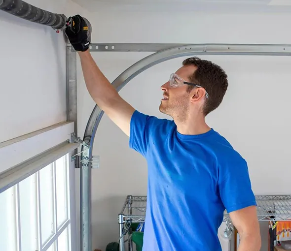 Technician in blue shirt inspecting and repairing a garage door spring indoors.