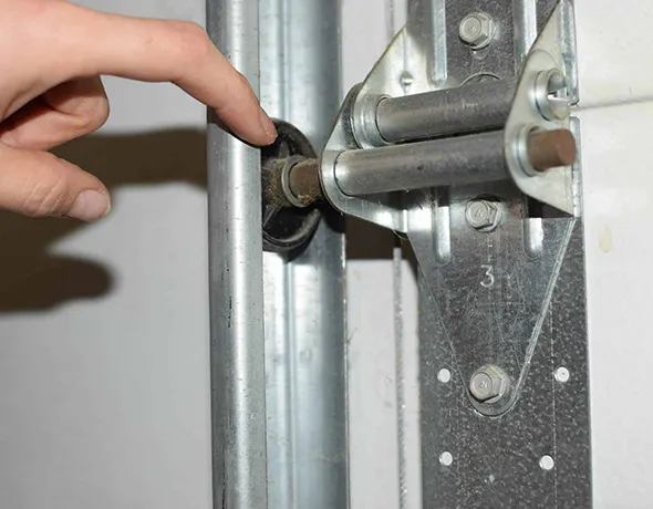 Hand reaching to replace or adjust a garage door roller on metal track.