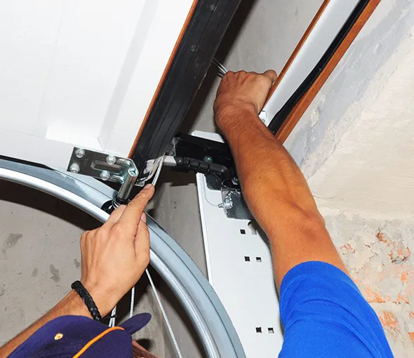 Technician adjusting and repairing garage door track with tools.